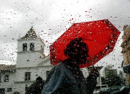Red - woman with red umbrella goes by car in traffic during rain.