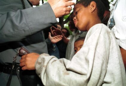 Playing with danger - boy tries to take gun from police officer while he talks with protesters.