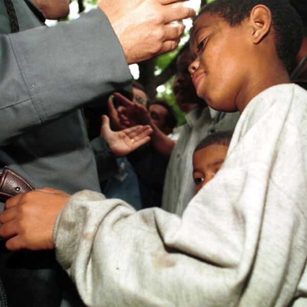Playing with danger - boy tries to take gun from police officer while he talks with protesters.
